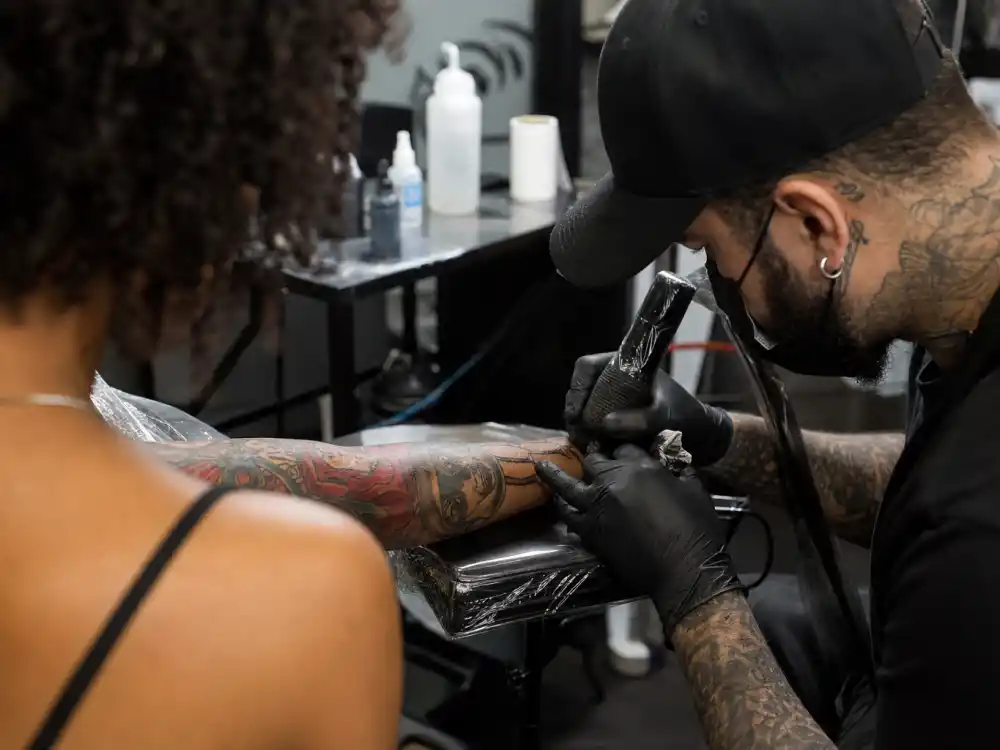 Neymar tattoos and their meanings studio session — tattoo artist gloved hands applying ink to forearm over-shoulder angle