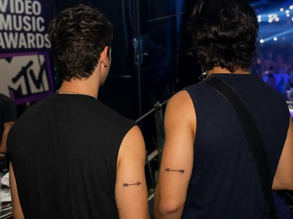 Nick Jonas tattoos and their meanings — matching arrow tattoo with brother Joe Jonas on back of arm at MTV awards backstage