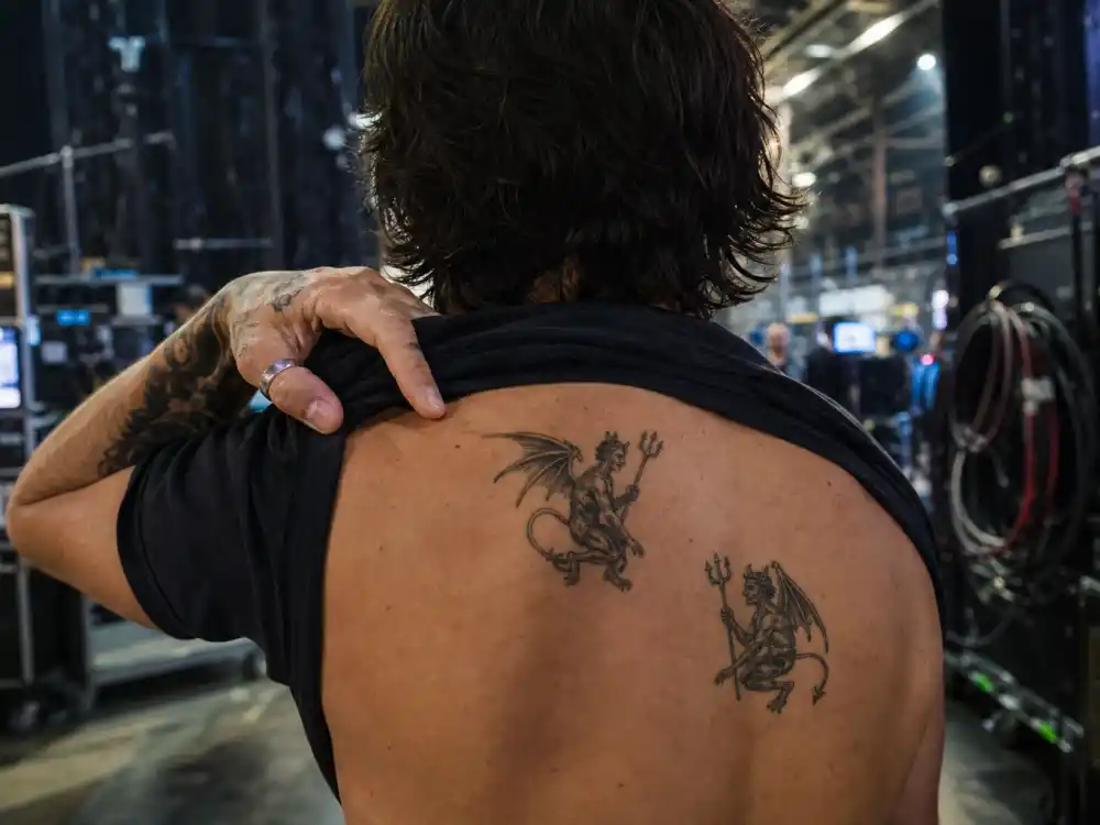 Norman Reedus tattoos and their meanings — two demon figure tattoos on right shoulder blade backstage TV set