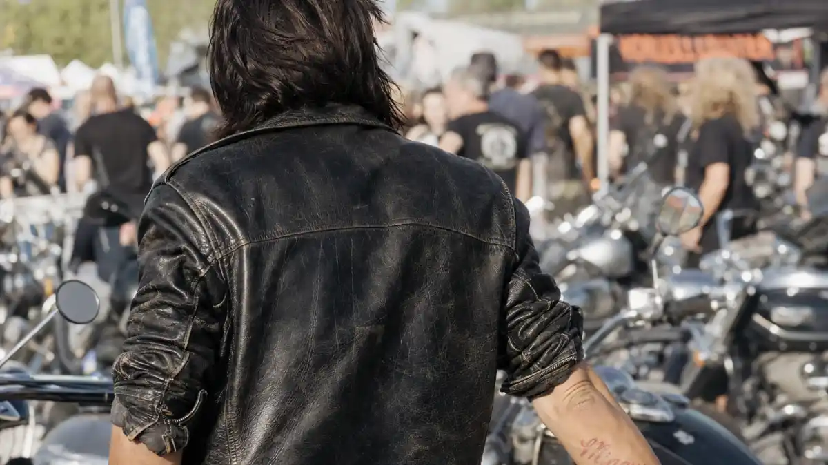 Norman Reedus tattoos and their meanings — actor from behind at motorcycle rally with red Mingus forearm script visible under leather jacket