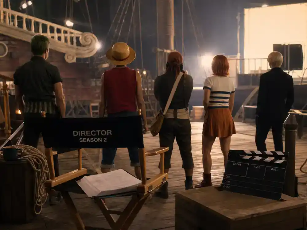 One Piece live action season 2 cast guide Straw Hat crew — actor silhouettes from behind rehearsing on pirate ship TV set with director chair and clapperboard