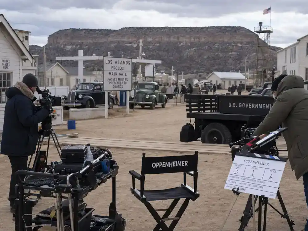 Oppenheimer movie filming locations guide Los Alamos — film crew on recreated 1940s military research compound with vintage cars and wooden barracks against New Mexico mesa backdrop