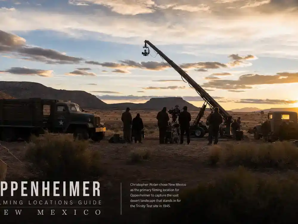 Oppenheimer movie filming locations guide New Mexico desert — camera crane and crew silhouettes against sunset mesa landscape with vintage period production trucks