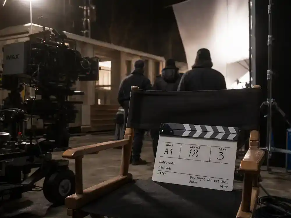 Oppenheimer movie filming locations guide Nolan production — IMAX camera rig and director chair on soundstage with crew silhouettes from behind and clapperboard on slate