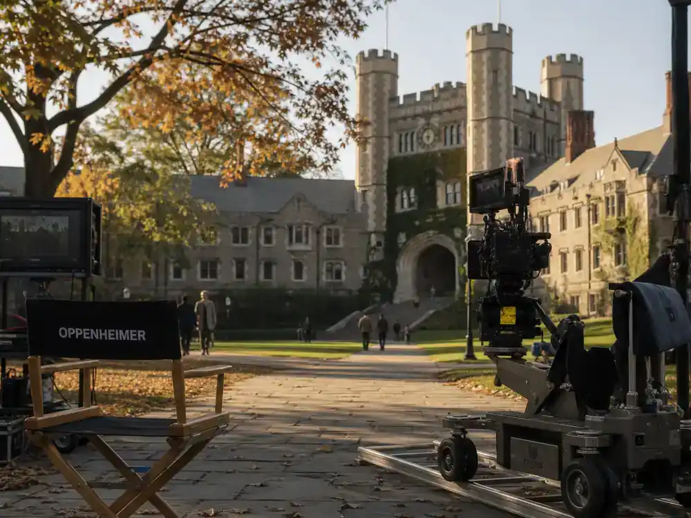 Oppenheimer movie filming locations guide Princeton campus — film crew on ivy-covered university quad with Gothic architecture, camera dolly, and director chair in autumn light