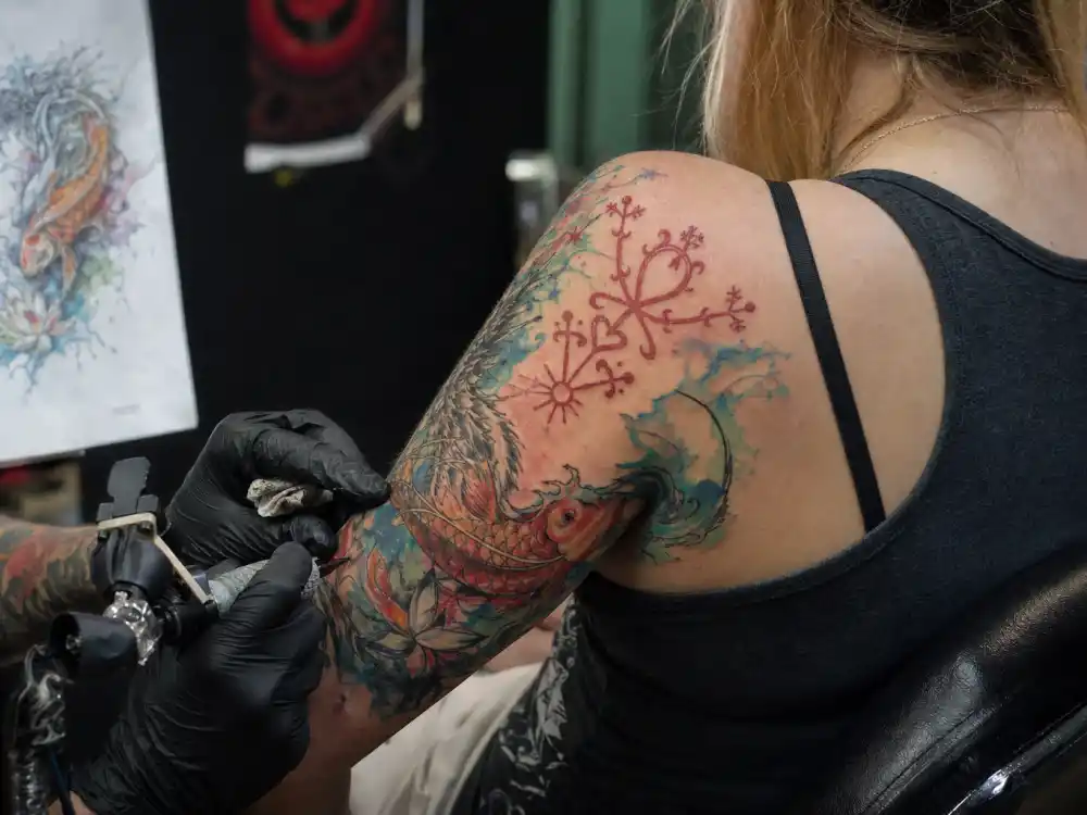 Paris Jackson tattoos and their meanings — tattoo artist inking red Vodou love symbol and watercolor dragon koi during studio session