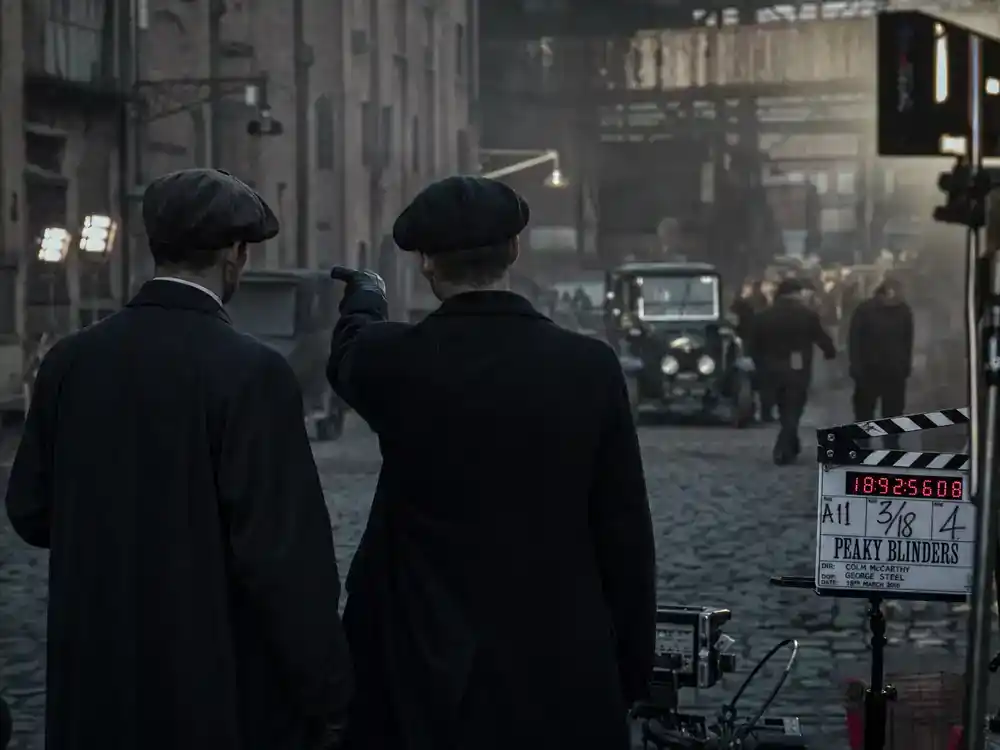 Peaky Blinders cast and real history guide Arthur Shelby — ensemble actor silhouettes rehearsing on gritty 1920s street film set from behind