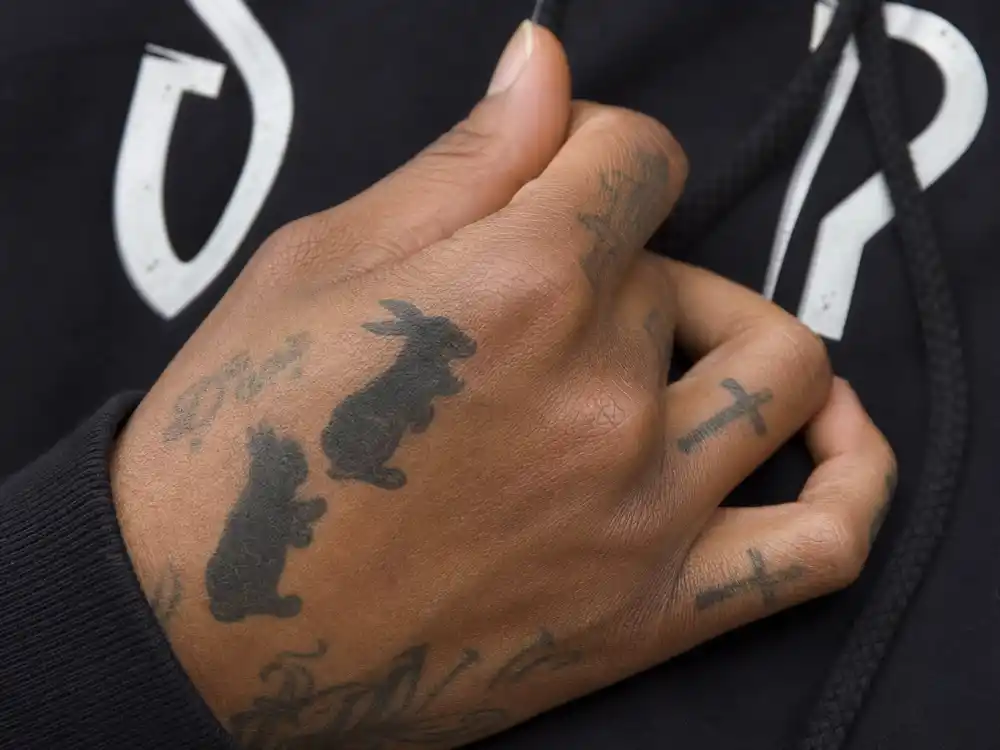Playboi Carti tattoos and their meanings — Donnie Darko rabbit silhouette hand tattoos and cross finger ink close-up