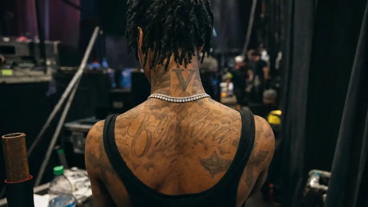 Playboi Carti tattoos and their meanings — Atlanta rapper from behind backstage with VLONE V neck tattoo and shoulder cross ink visible
