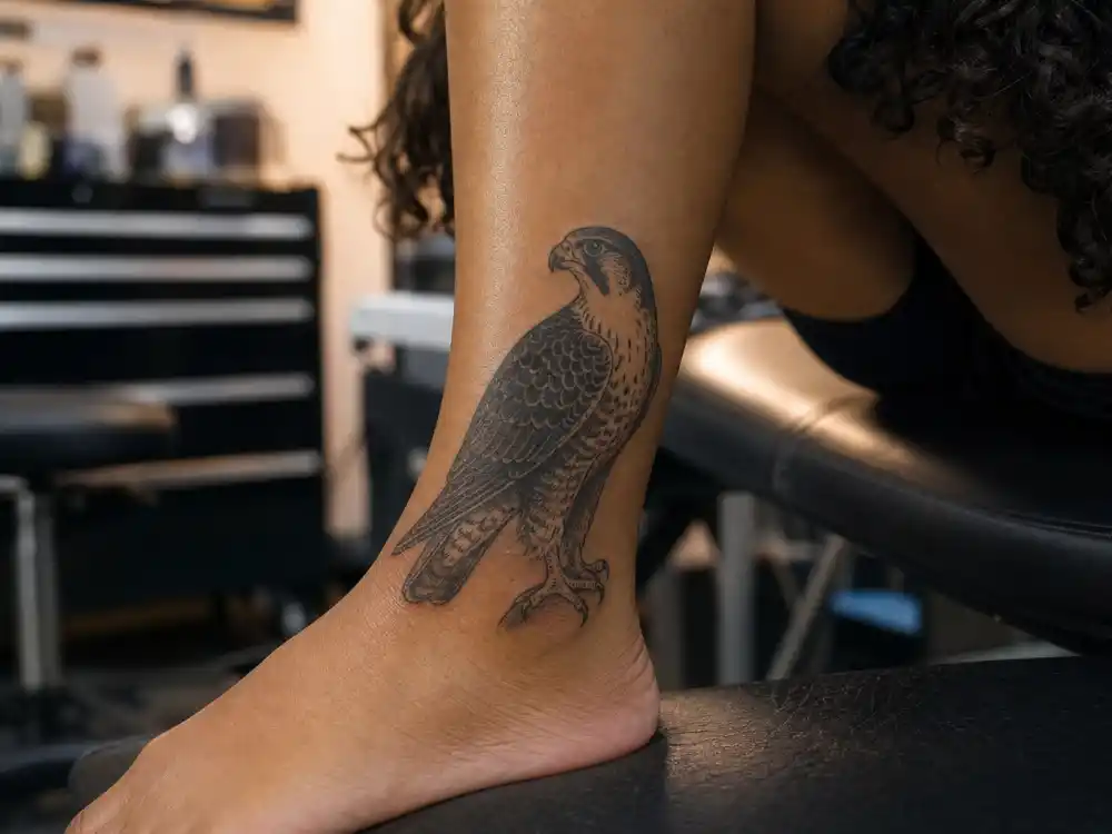 Rihanna tattoos and their meanings — detailed falcon bird tattoo on ankle with skull and music note ink visible in studio close-up
