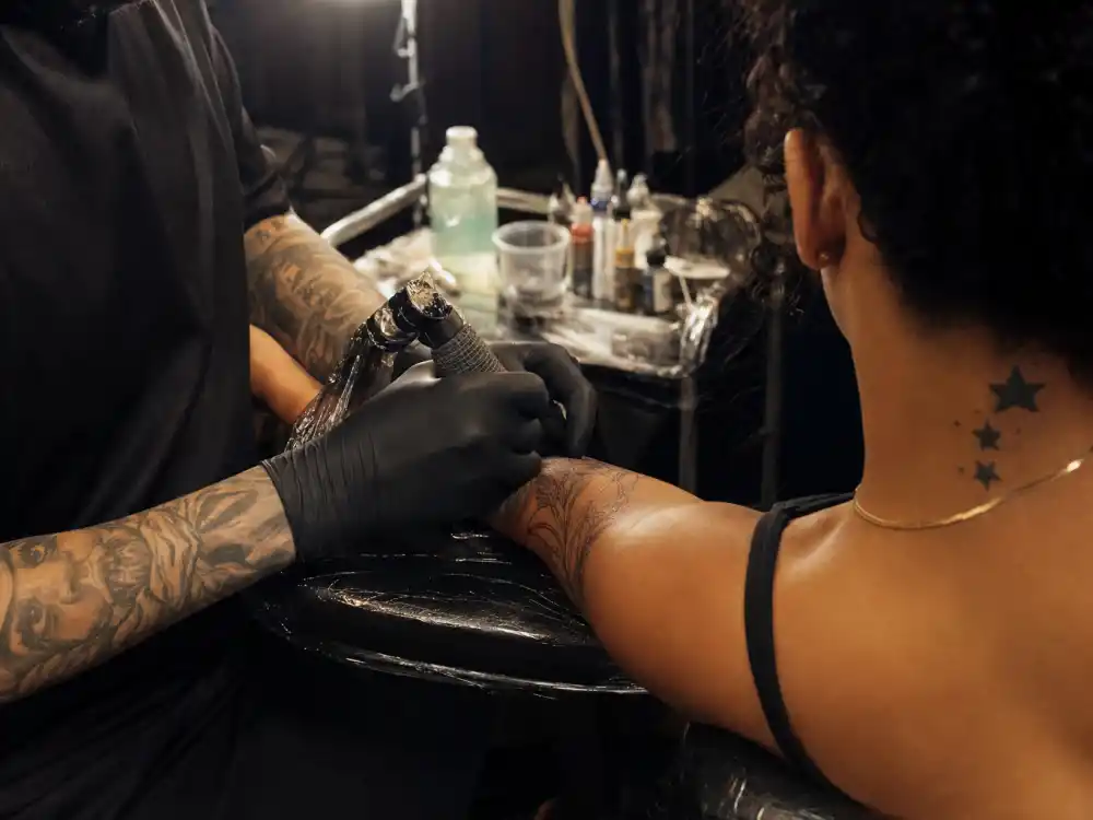 Rihanna tattoos and their meanings — tattoo artist inking forearm during professional studio session with stars visible on client neck