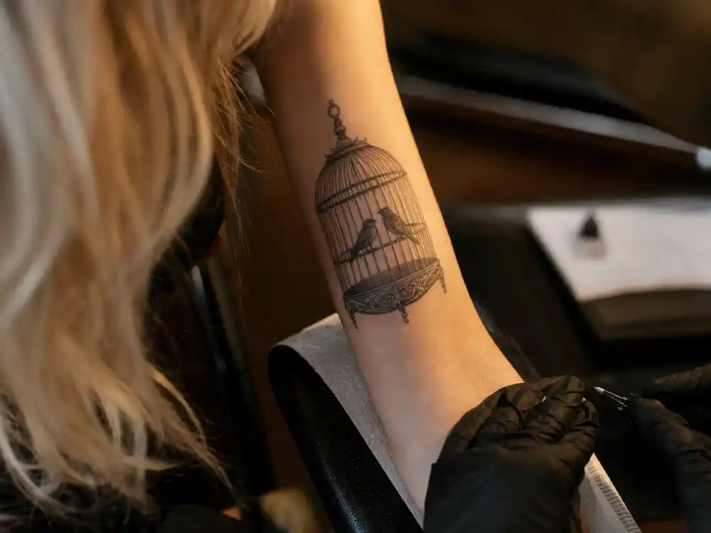 Rita Ora tattoos and their meanings birdcage arm — two birds inside cage fine-line tattoo on inner right arm protecting love symbolism