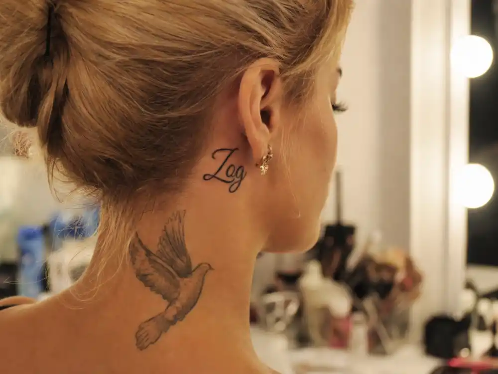Rita Ora tattoos and their meanings Zog neck — Albanian pet name cursive tattoo under ear plus dove ink on nape from mother Vera