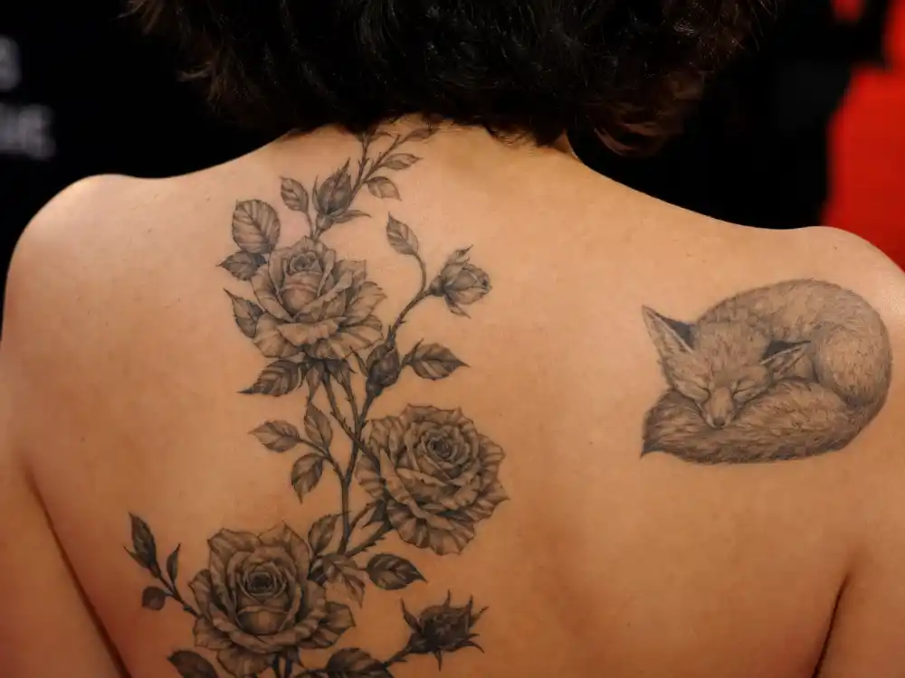 Scarlett Johansson tattoos and their meanings — detailed rose vine and resting lamb tattoo on upper back photographed at premiere