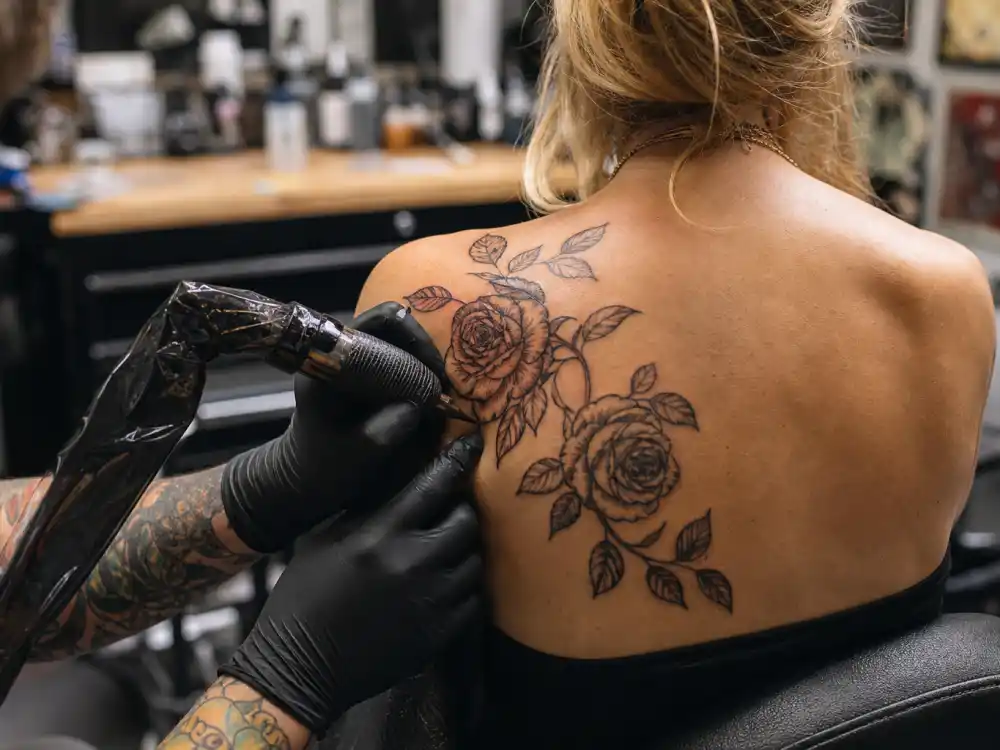 Scarlett Johansson tattoos and their meanings — tattoo artist inking rose vine back design during professional studio session