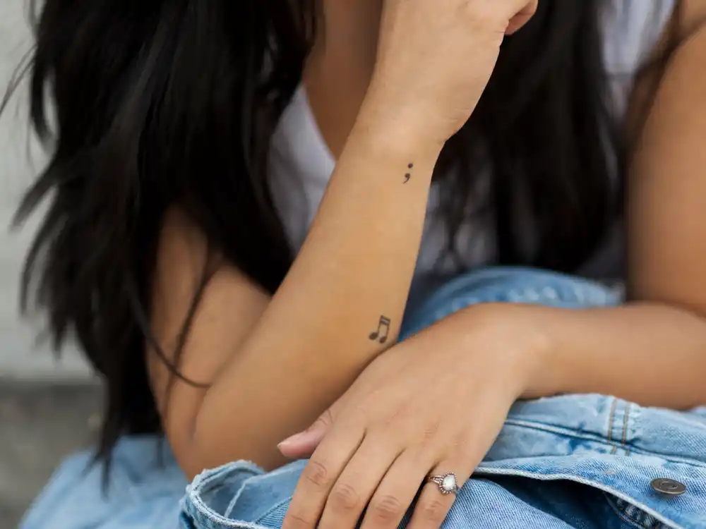 Selena Gomez tattoos and their meanings — semicolon and music note wrist tattoos photographed in natural daylight
