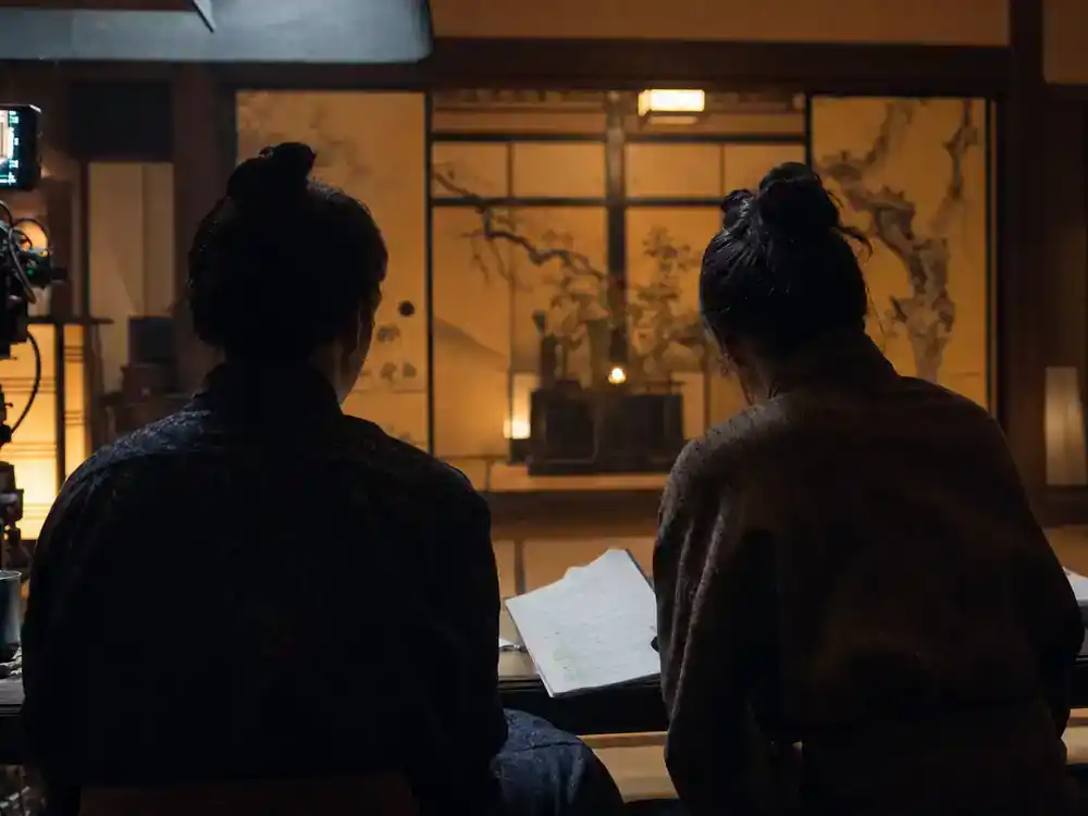 Shogun FX cast and characters guide Mariko — two actor silhouettes rehearsing emotional scene on Japanese period drama interior set with paper screens and warm lantern light