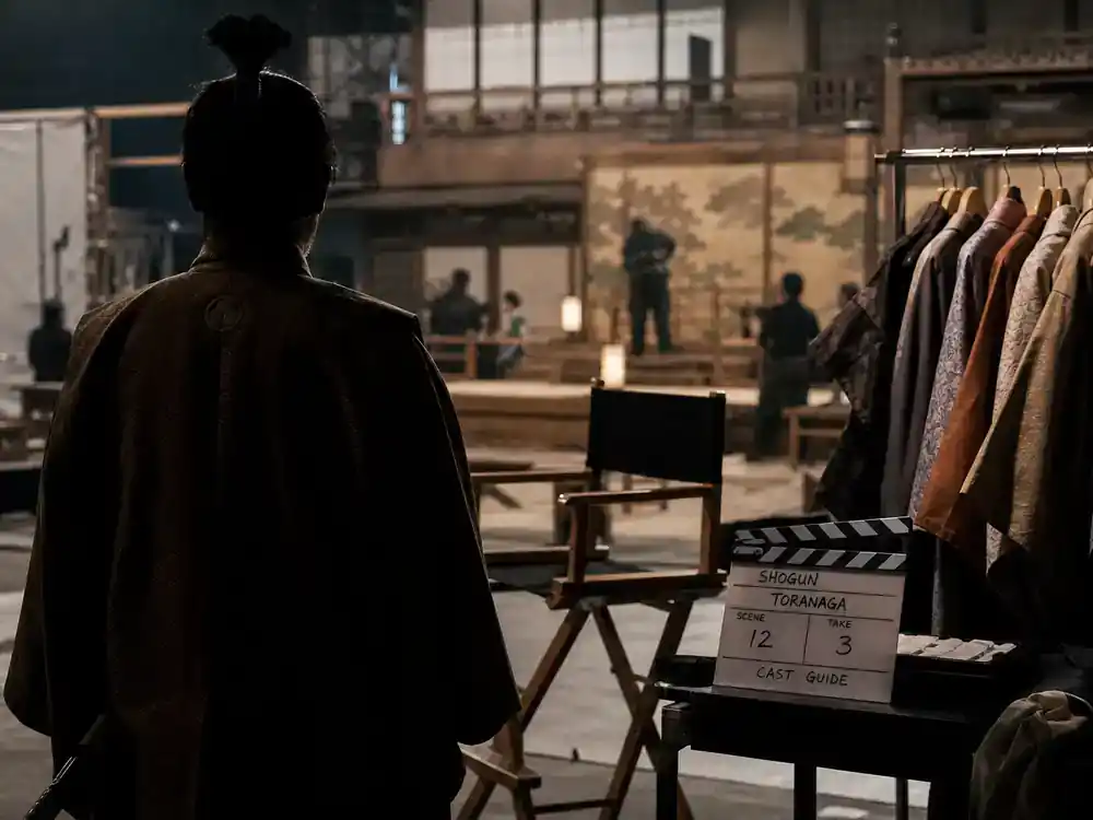 Shogun FX cast and characters guide Toranaga — lead actor silhouette from behind in samurai-era costume on historical TV drama soundstage with director chair