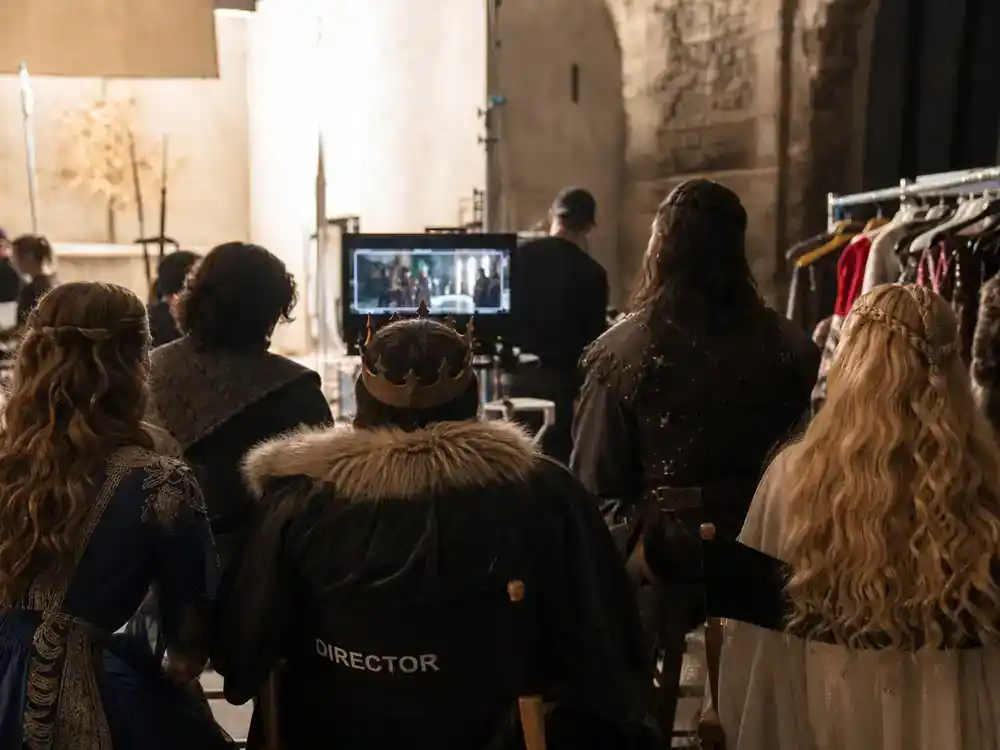 Snow White 2026 movie cast and controversy explained ensemble cast — performer silhouettes on medieval fantasy film set from behind with costume rack