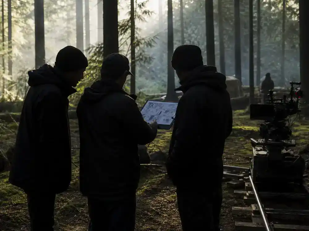 Snow White 2026 movie cast and controversy explained filming — forest location scouting with crew silhouettes reviewing storyboard among pine trees