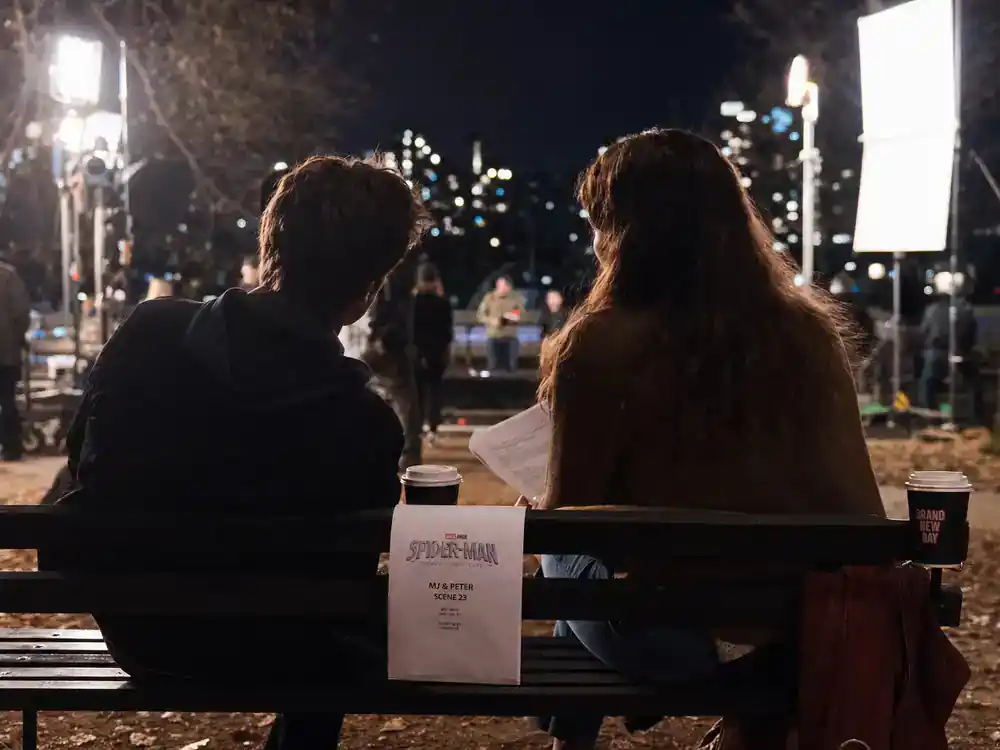 Spider-Man Brand New Day cast and characters guide MJ scene — two actor silhouettes on park bench during night shoot rehearsal, faces turned away