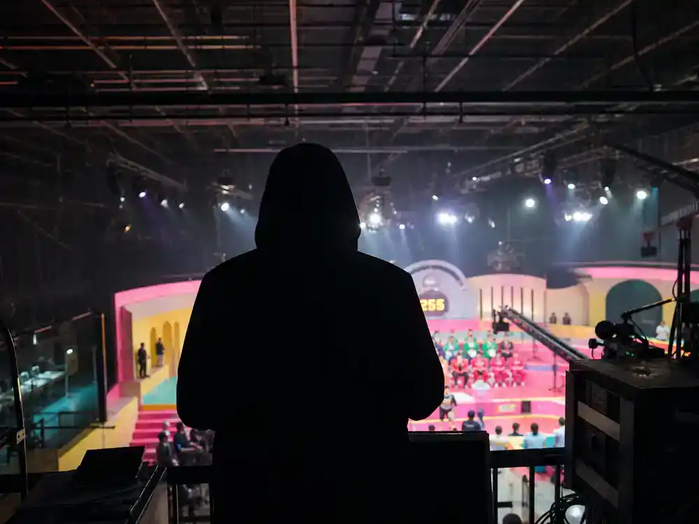 Squid Game cast and characters explained Front Man — hooded figure silhouette from behind on elevated platform overlooking colorful TV game set below