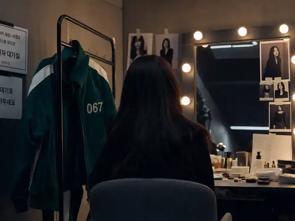 Squid Game cast and characters explained Sae-byeok — actress silhouette from behind at makeup mirror with green tracksuit on wardrobe rack in casting room
