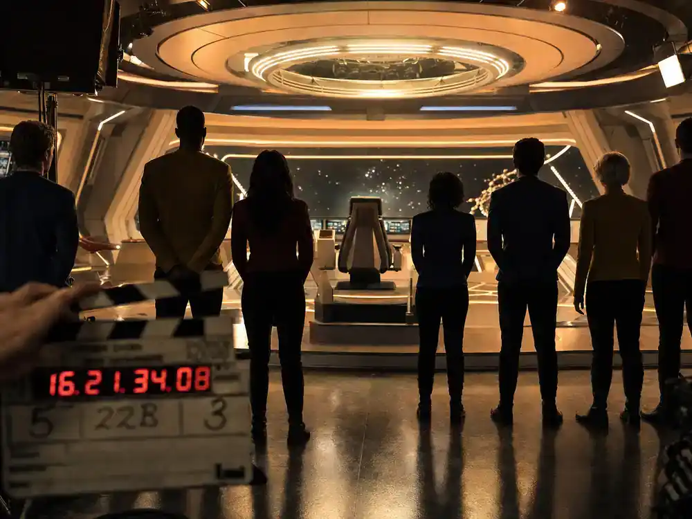 Star Trek universe 2026 shows and cast guide Pike crew — ensemble cast silhouettes from behind on sci-fi TV bridge set with clapperboard and warm production lighting