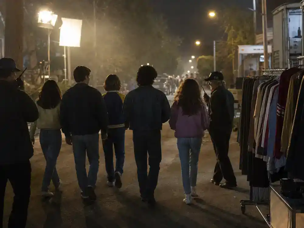 Stranger Things season 5 cast and characters guide Hawkins kids — teen actor silhouettes from behind rehearsing on suburban street film set with 1980s wardrobe racks
