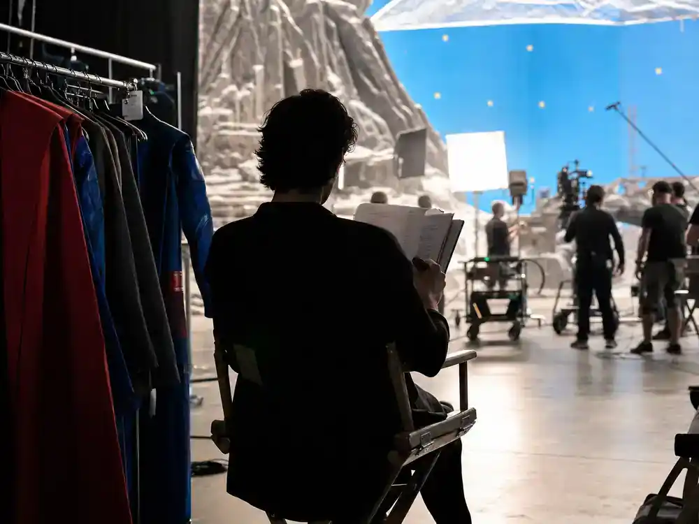 Superman 2026 movie cast and characters guide David Corenswet — actor silhouette reviewing script on director chair from behind on superhero film set