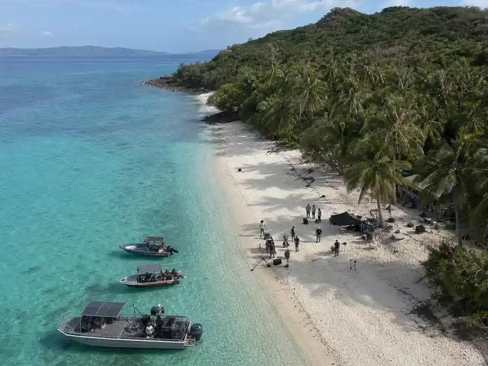 Survivor 50 cast and season preview guide Fiji — Mamanuca Islands filming location with production boats turquoise water and camera crew on beach