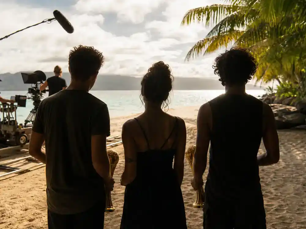 Survivor 50 cast and season preview guide winners — three returning Sole Survivor silhouettes on Fiji beach film set with golden trophy prop