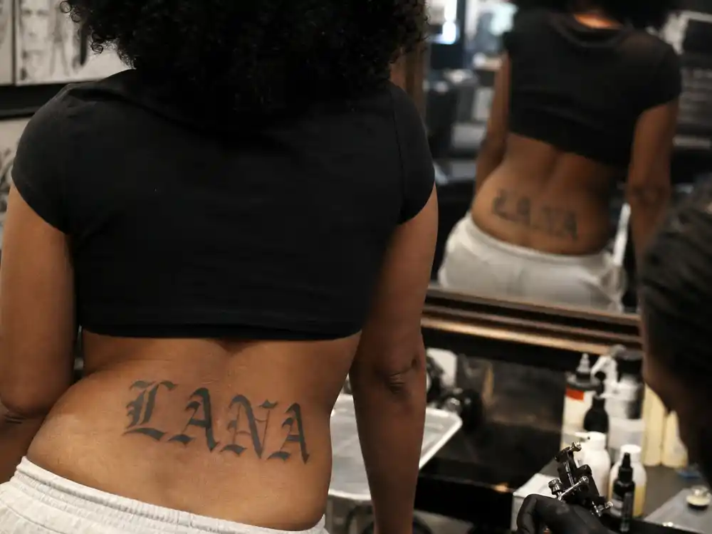 SZA tattoos and their meanings Lana — gothic Old English LANA script tattoo on lower back in studio mirror over-shoulder close-up
