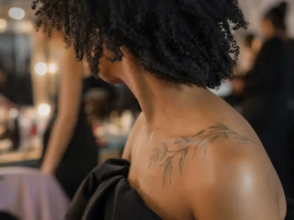 SZA tattoos and their meanings maple leaf — delicate leaf and branch tattoo on collarbone backstage over-shoulder angle