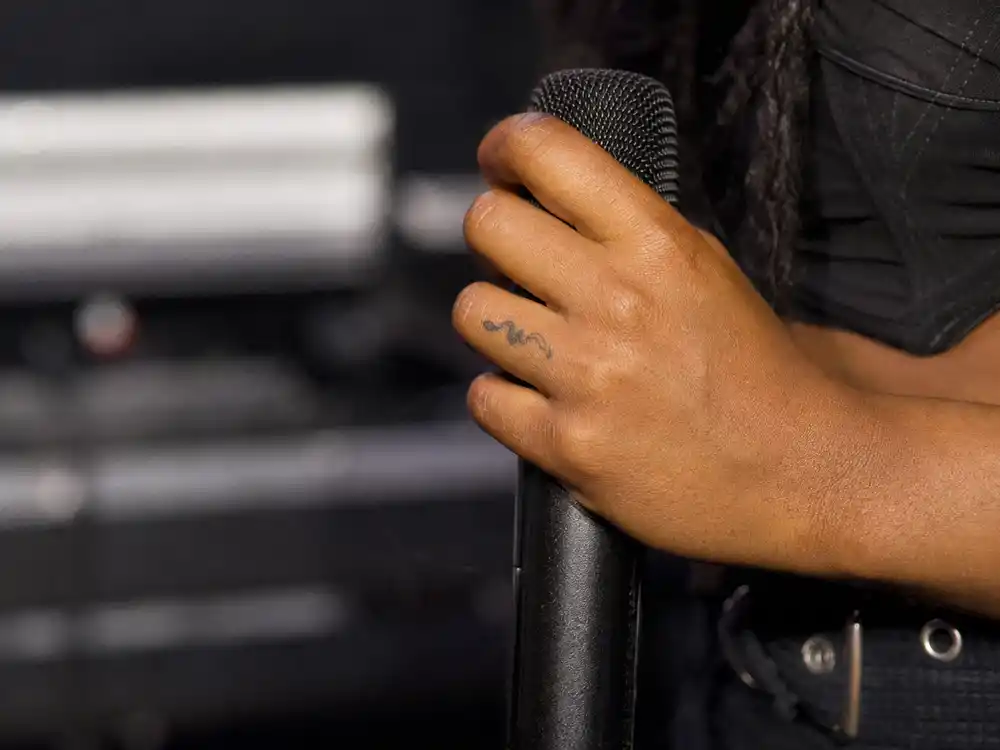 SZA tattoos and their meanings snake — tiny snake tattoo on pinkie finger close-up holding microphone backstage