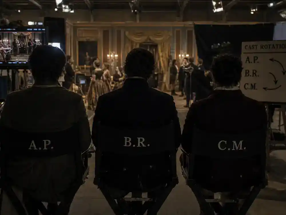The Crown cast vs real royals guide cast rotation — three actor silhouettes from behind on director chairs on royal period drama soundstage