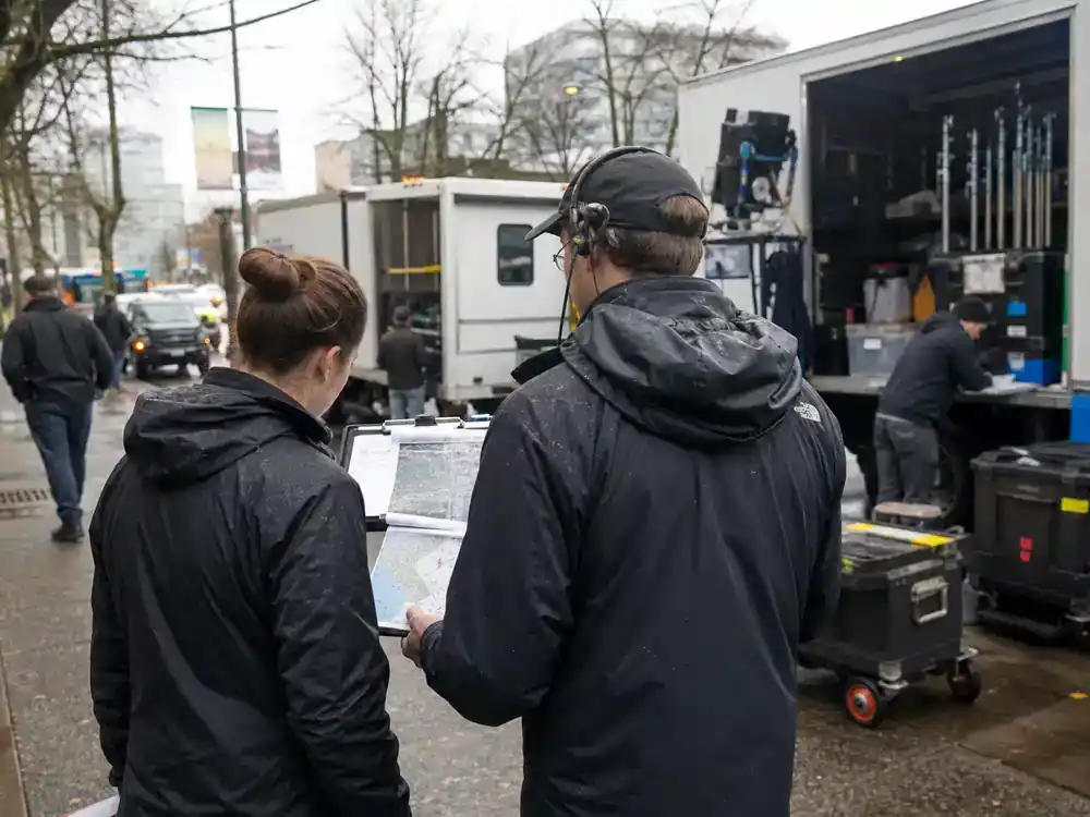 The Last of Us behind the scenes filming facts Vancouver filming — crew from behind reviewing location maps beside film trucks on rainy urban street