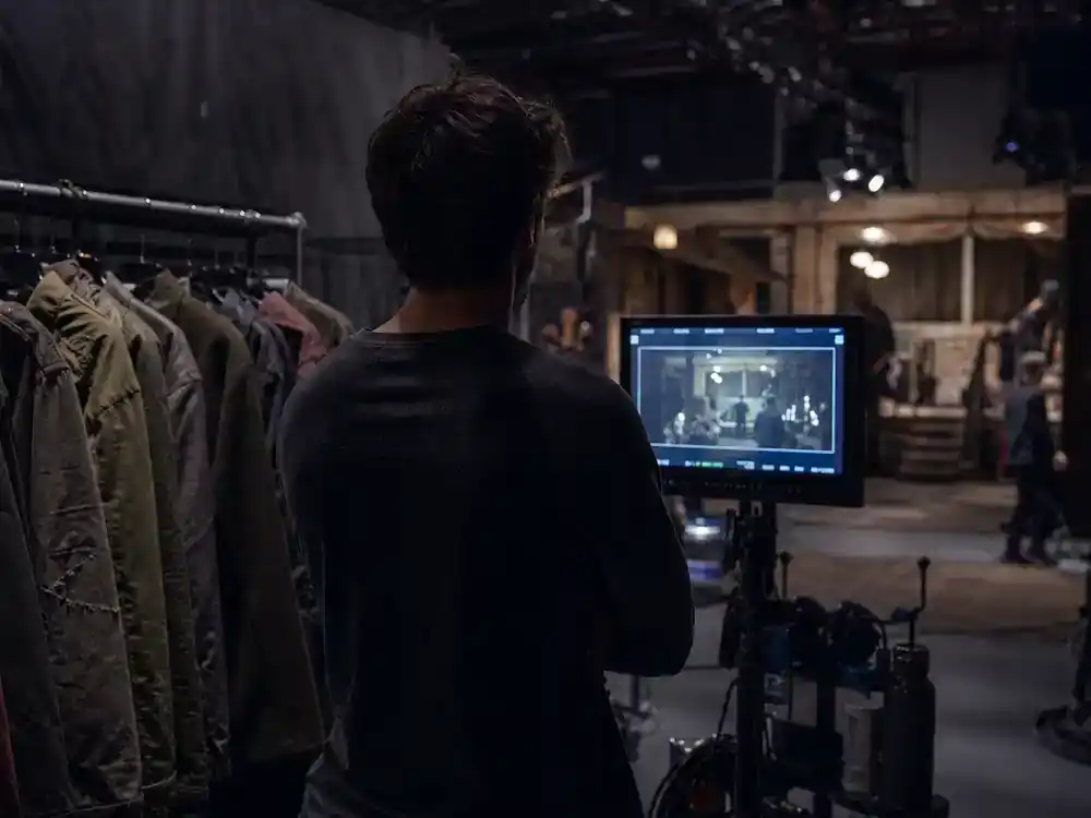 The Last of Us season 2 cast and episode guide Bella Ramsey Ellie — young actor silhouette rehearsing on soundstage with wardrobe rack and director monitor
