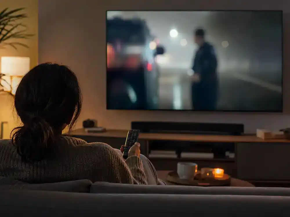 The Last of Us season 2 cast and episode guide HBO release — viewer from behind on couch watching premium cable drama on living room TV during weekly premiere night