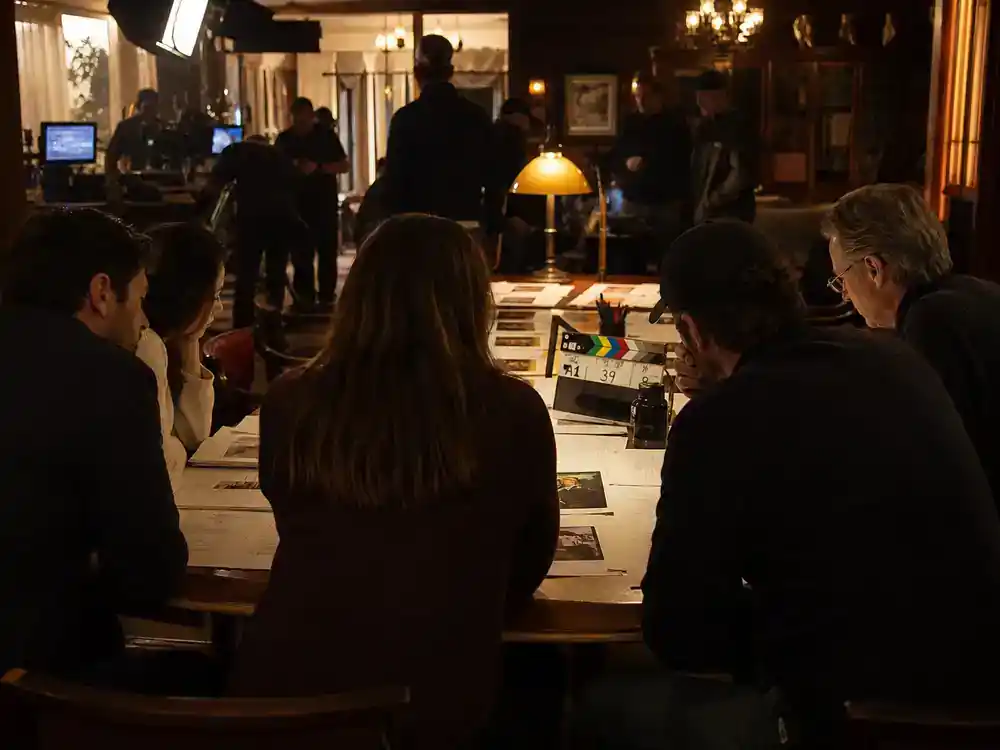 The Last of Us season 2 cast and episode guide returning cast — ensemble silhouettes reviewing episode breakdown printouts at production table on set