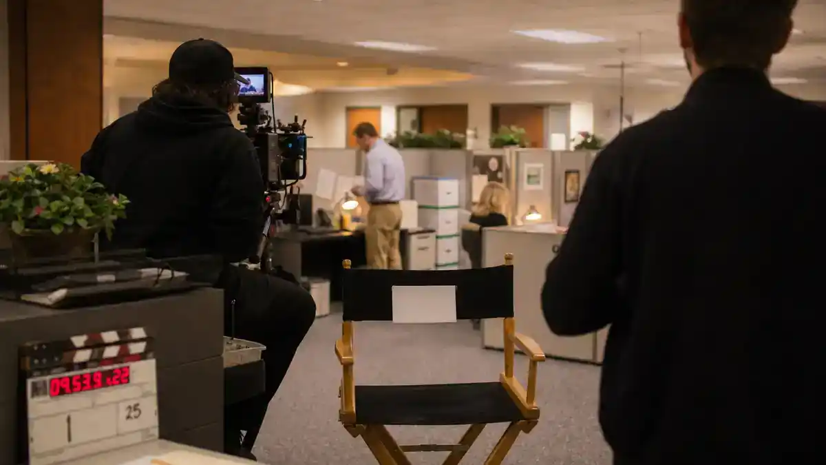The Office cast net worth 2026 ranked — generic corporate office TV set with cubicles, clapperboard and director chair, editorial production reference