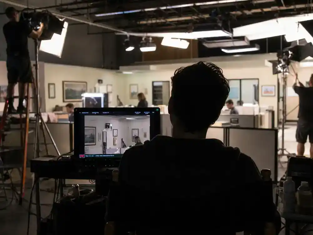 The Office cast net worth 2026 ranked John Krasinski Jim Halpert — actor silhouette at camera monitor on office sitcom soundstage