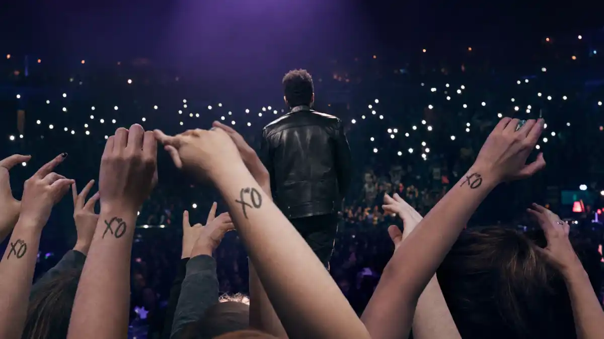 The Weeknd tattoos and their meanings — R&B singer from behind on concert stage with fan XO wrist tattoos visible in crowd