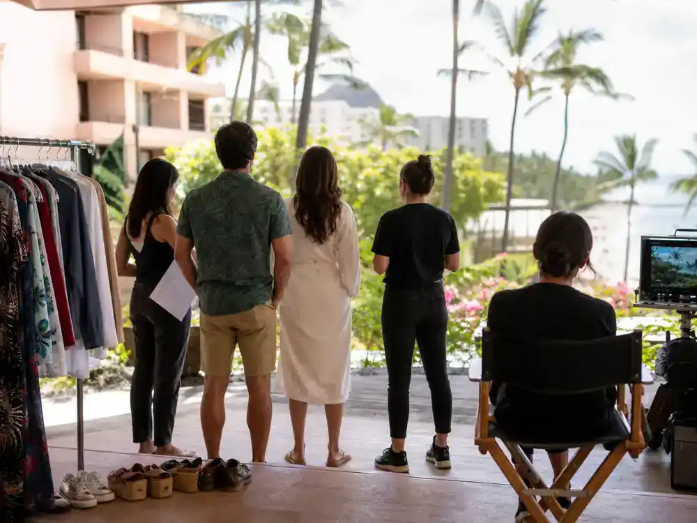 The White Lotus filming locations season guide Hawaii — TV drama cast silhouettes from behind on tropical resort film set with wardrobe racks at Maui-style beach hotel terrace