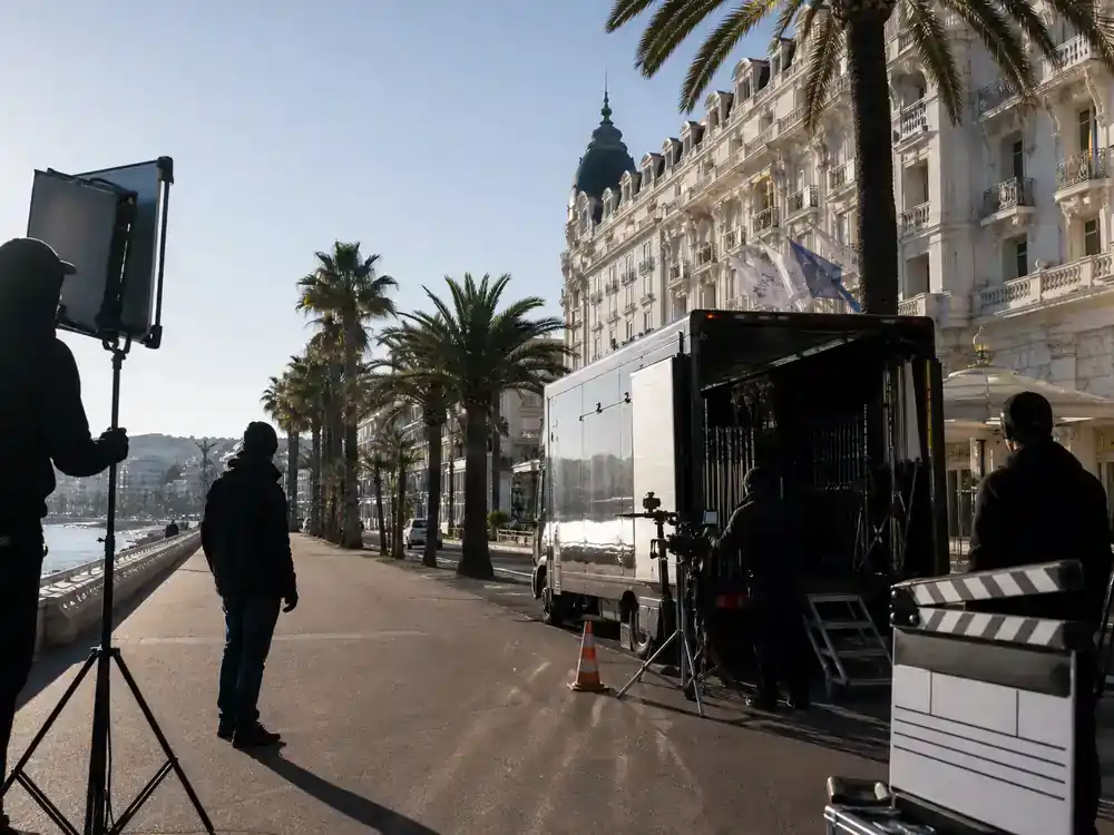 The White Lotus filming locations season guide French Riviera — film production trucks and crew on coastal luxury hotel exterior Mediterranean promenade location scout