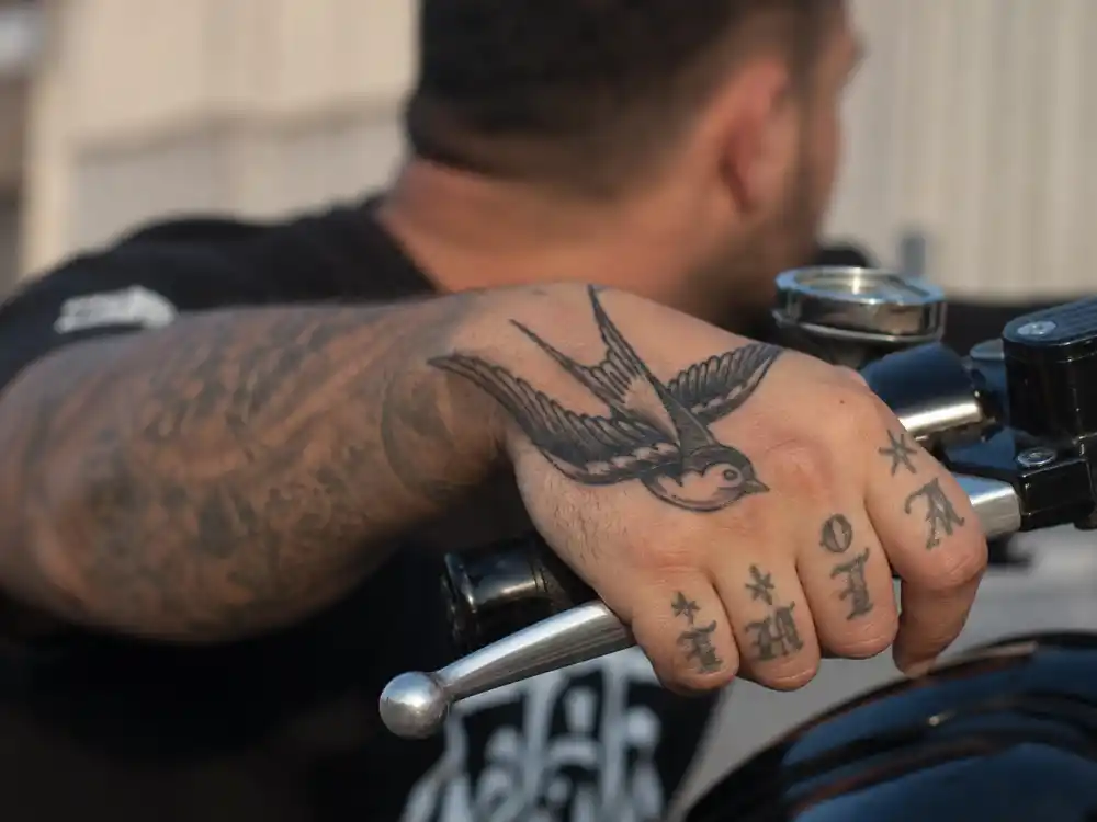 Tom Hardy tattoos and their meanings — traditional swallow hand tattoo on motorcycle handlebar grip close-up