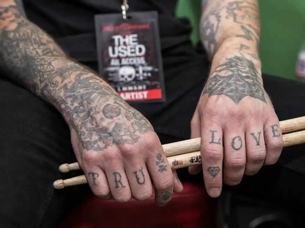 Travis Barker tattoos and their meanings — tattooed fingers and knuckles with letter ink on drummer hands holding sticks backstage