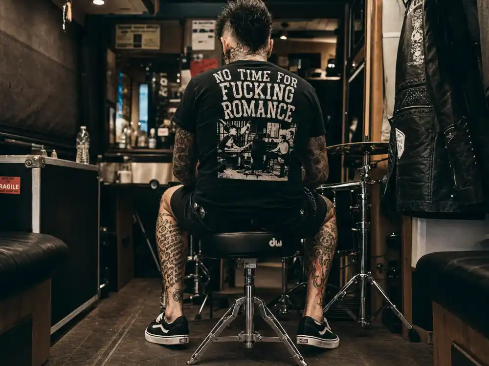 Travis Barker tattoos and their meanings — tattooed legs and feet with script and flame ink on punk drummer from behind backstage