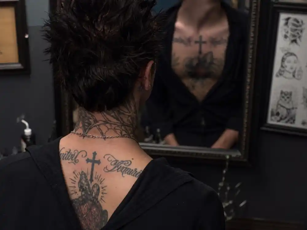 Travis Barker tattoos and their meanings — neck and chest cross and script tattoos visible over-shoulder on punk rock musician