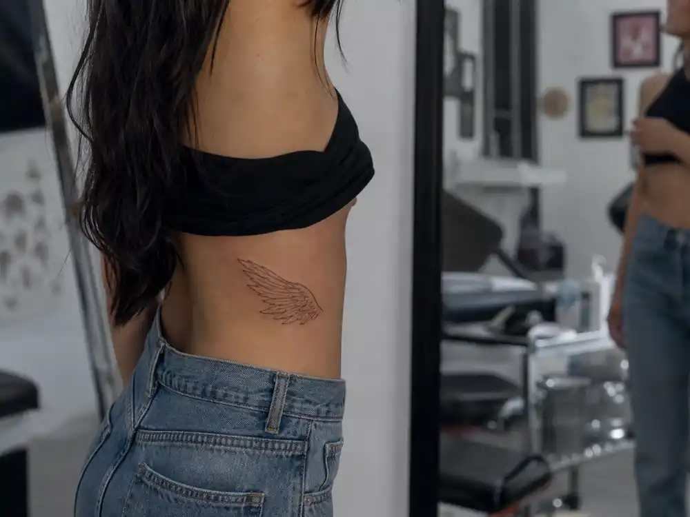 Vanessa Hudgens tattoos and their meanings — delicate divine feminine angel wing tattoo on right side torso above hip